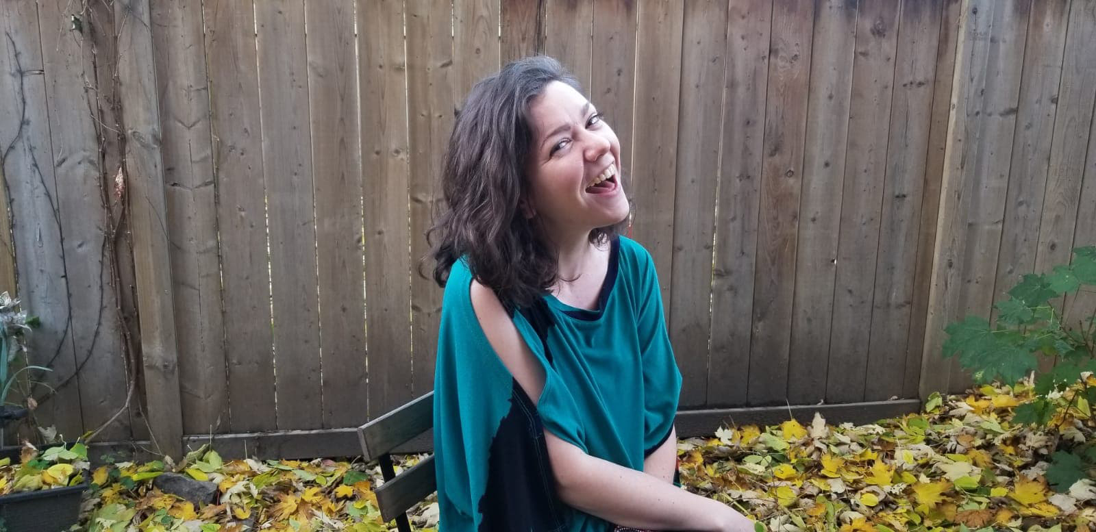 Hannah sits outside in autumn, smiling in front of a wooden fence.