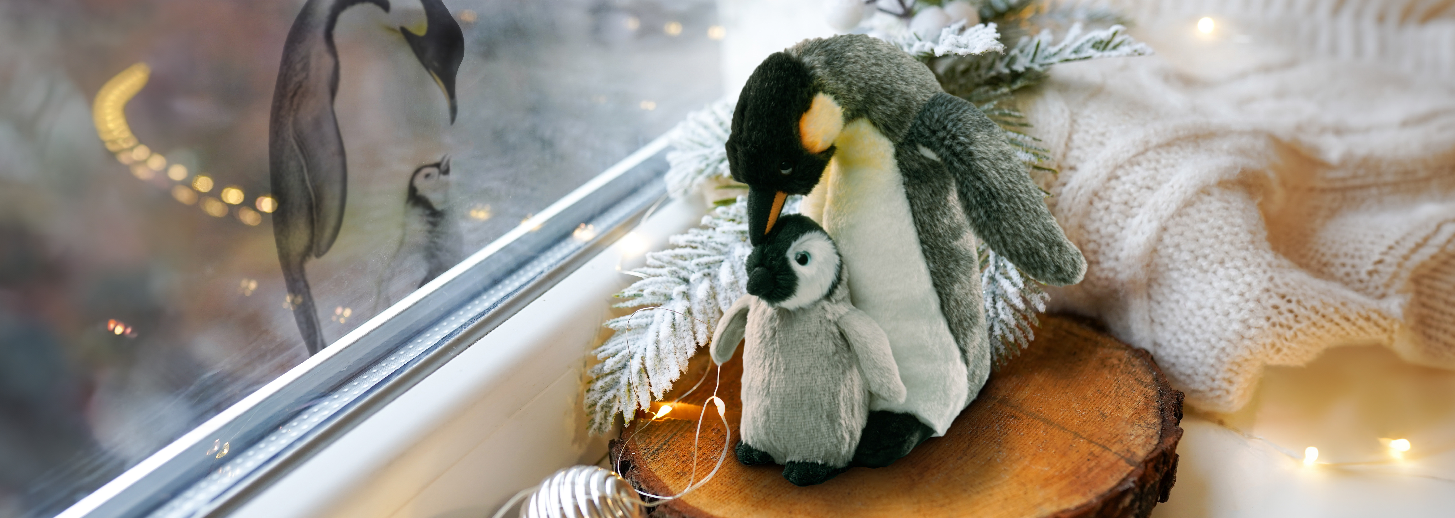 Image of plush penguin near a window, with a reflection of a real penguin in the glass.