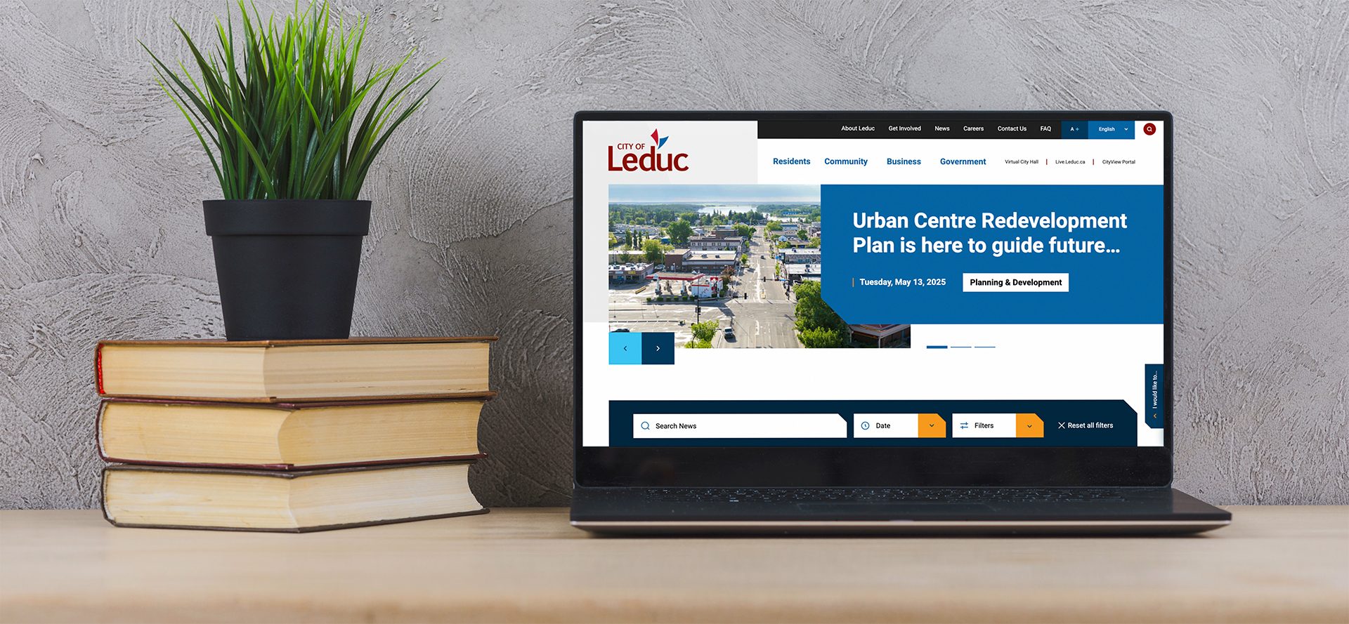 Laptop on a desk next to books and a plant, showing the Leduc News page.