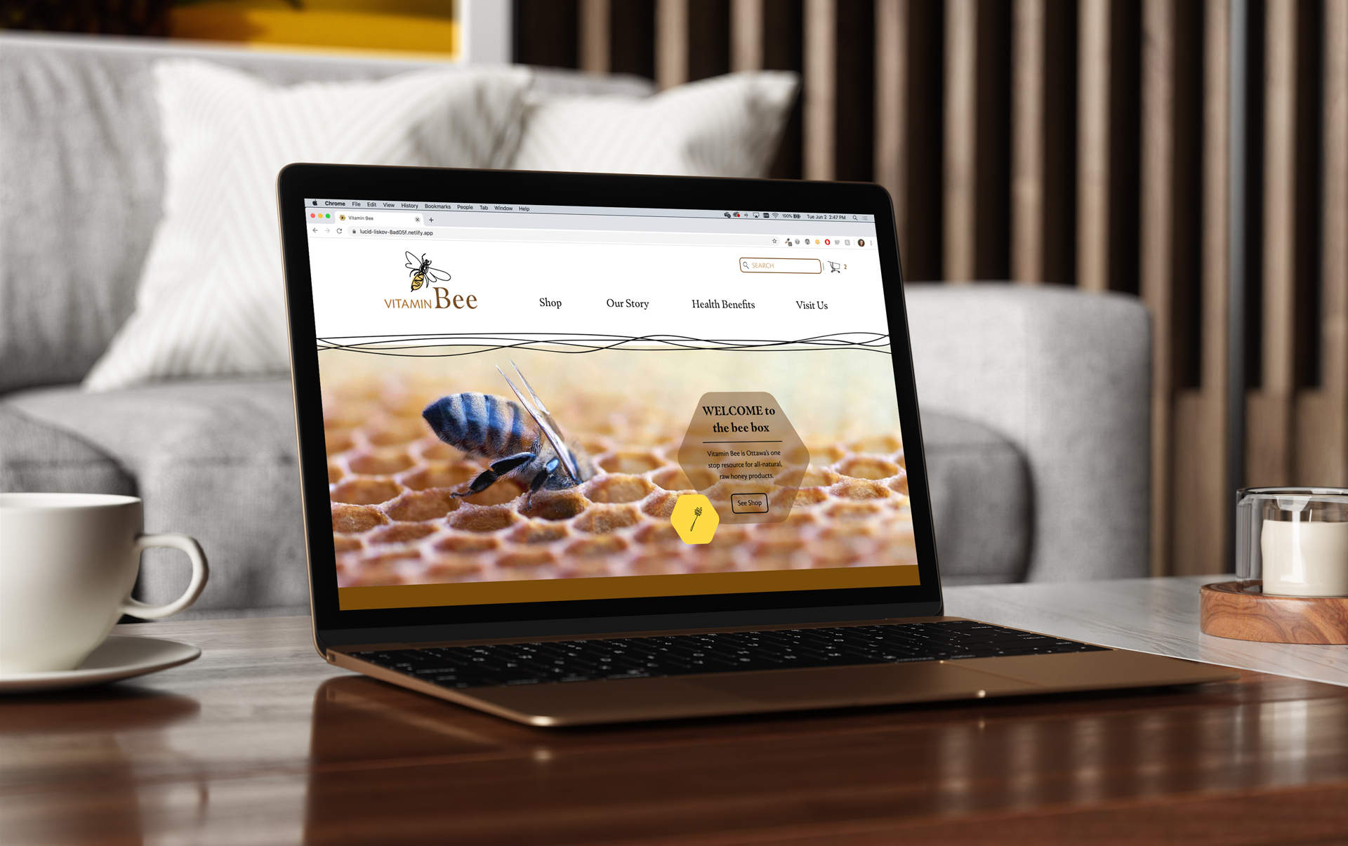 A laptop showing the Vitamin Bee homepage sitting on a coffee table, with a teacup, candle and white couch in the background.